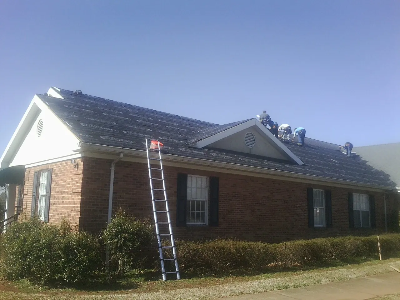Crew tearing shingles off a brick ranch roof with a ladder set — Metal Roof Repair work by our crew in Narberth