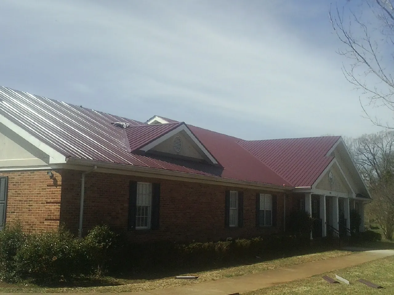 Red metal roof with gabled entries on a long brick building, from a Hail Damage Roof Repair job in Narberth